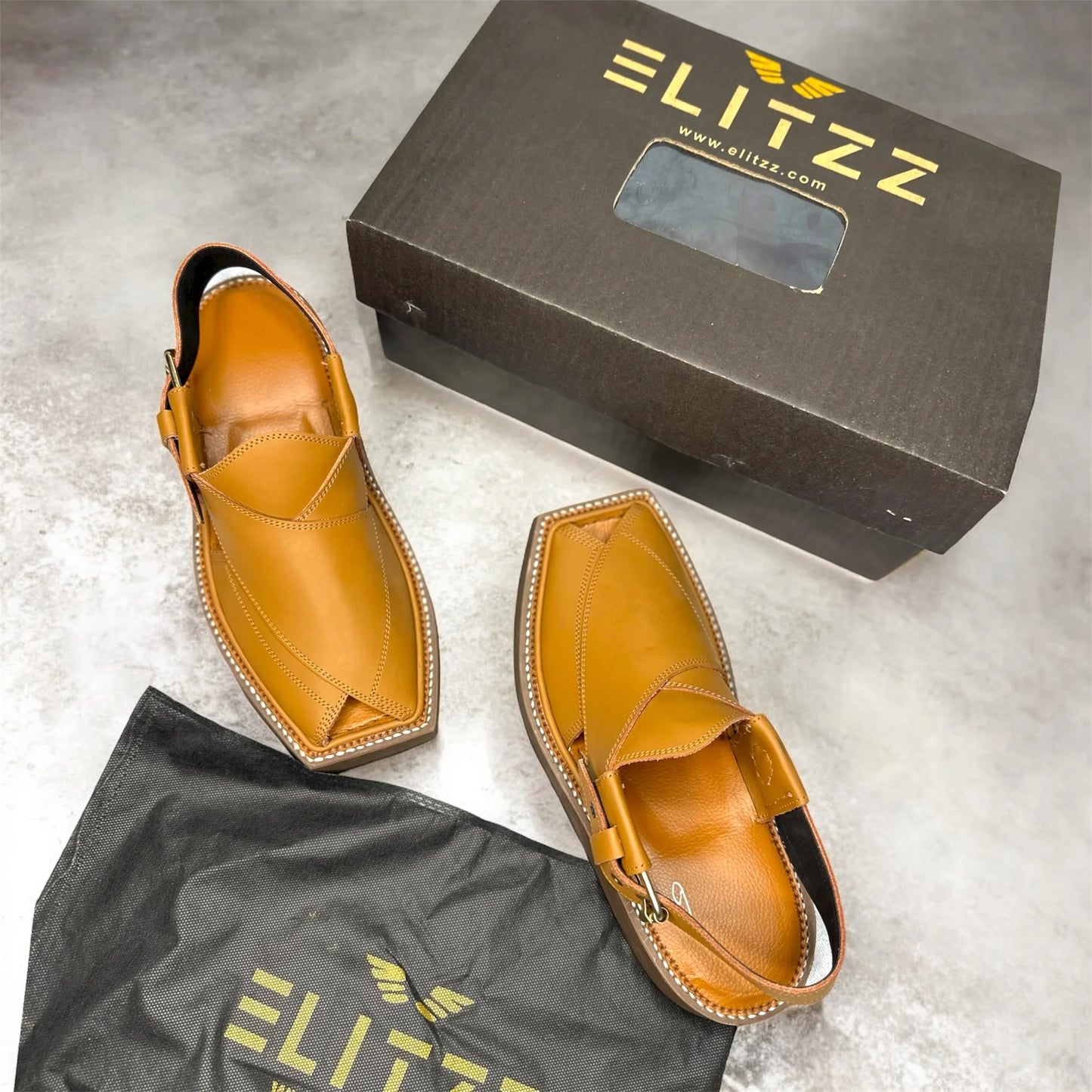 Pair of tan leather Elitzz men's traditional sandals with open toes, displayed with branded shoe box and dust bag on gray surface