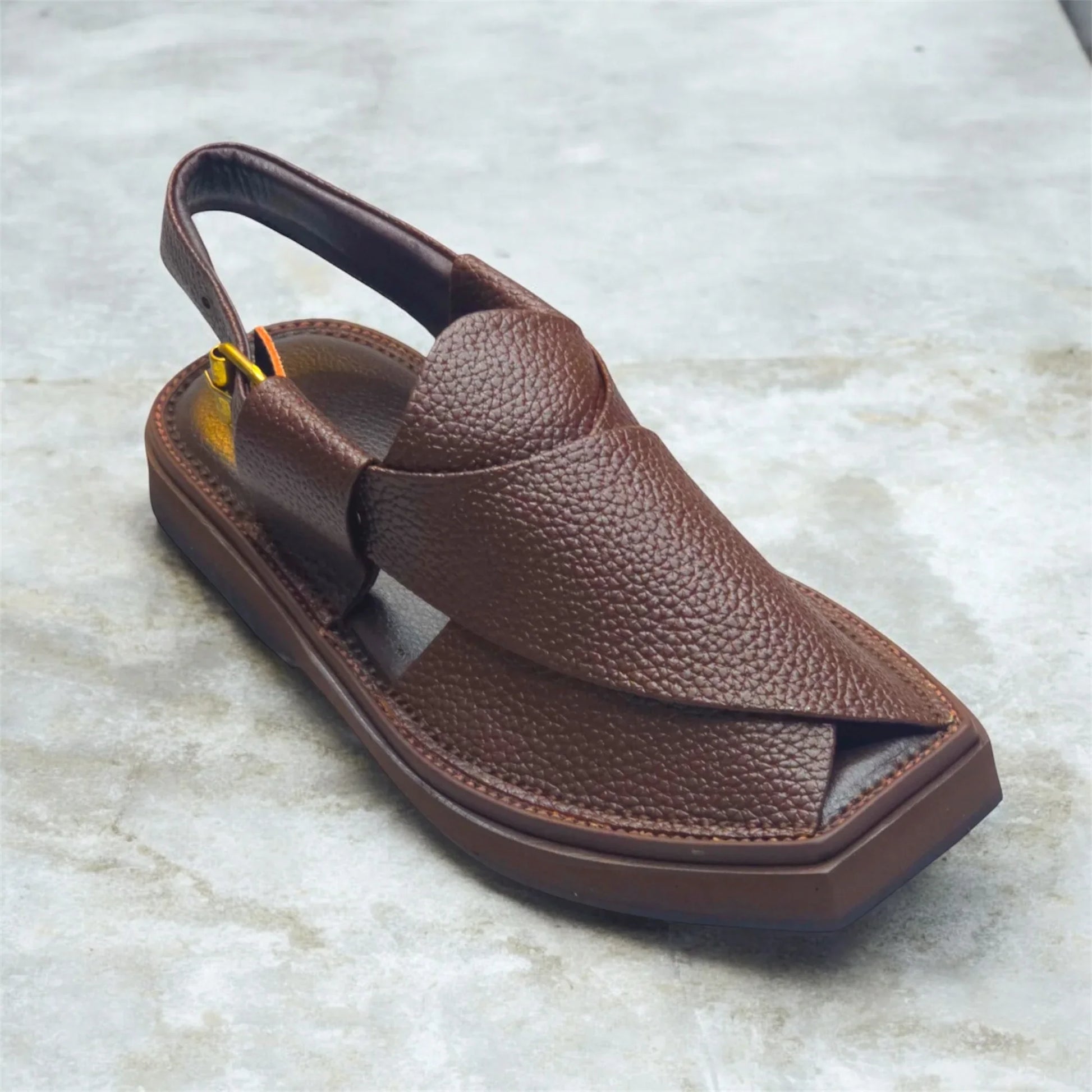 Brown leather men's sandal with textured upper and slingback strap on concrete floor